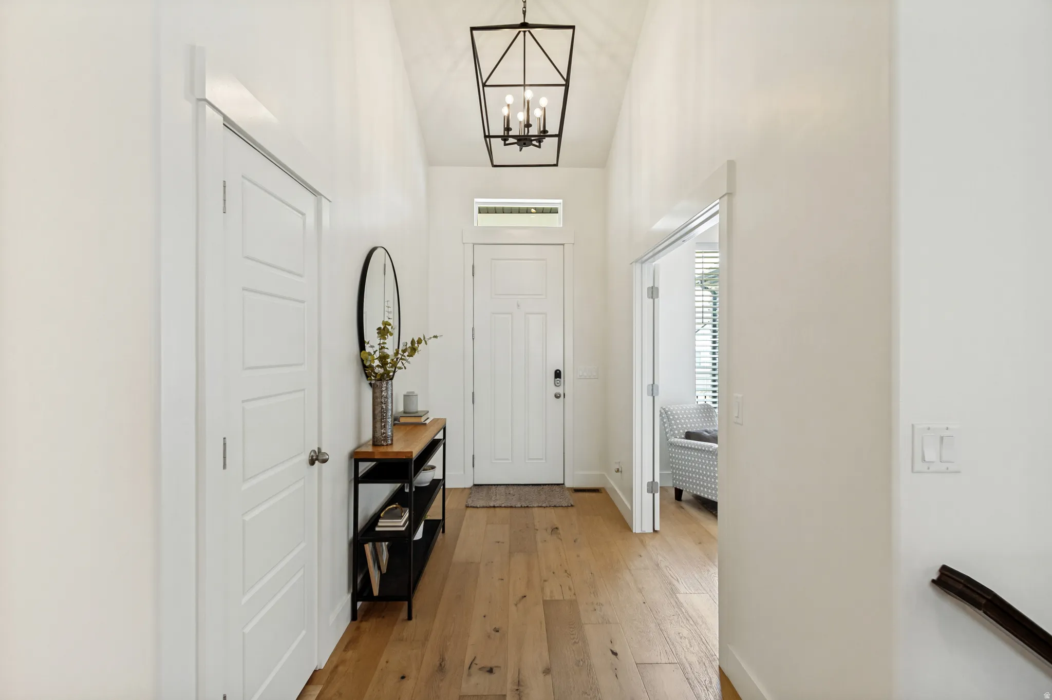 Vaulted entryway featuring wood-finish flooring, a contemporary black metal chandelier, a panel front door with transom window, and a paneled interior door