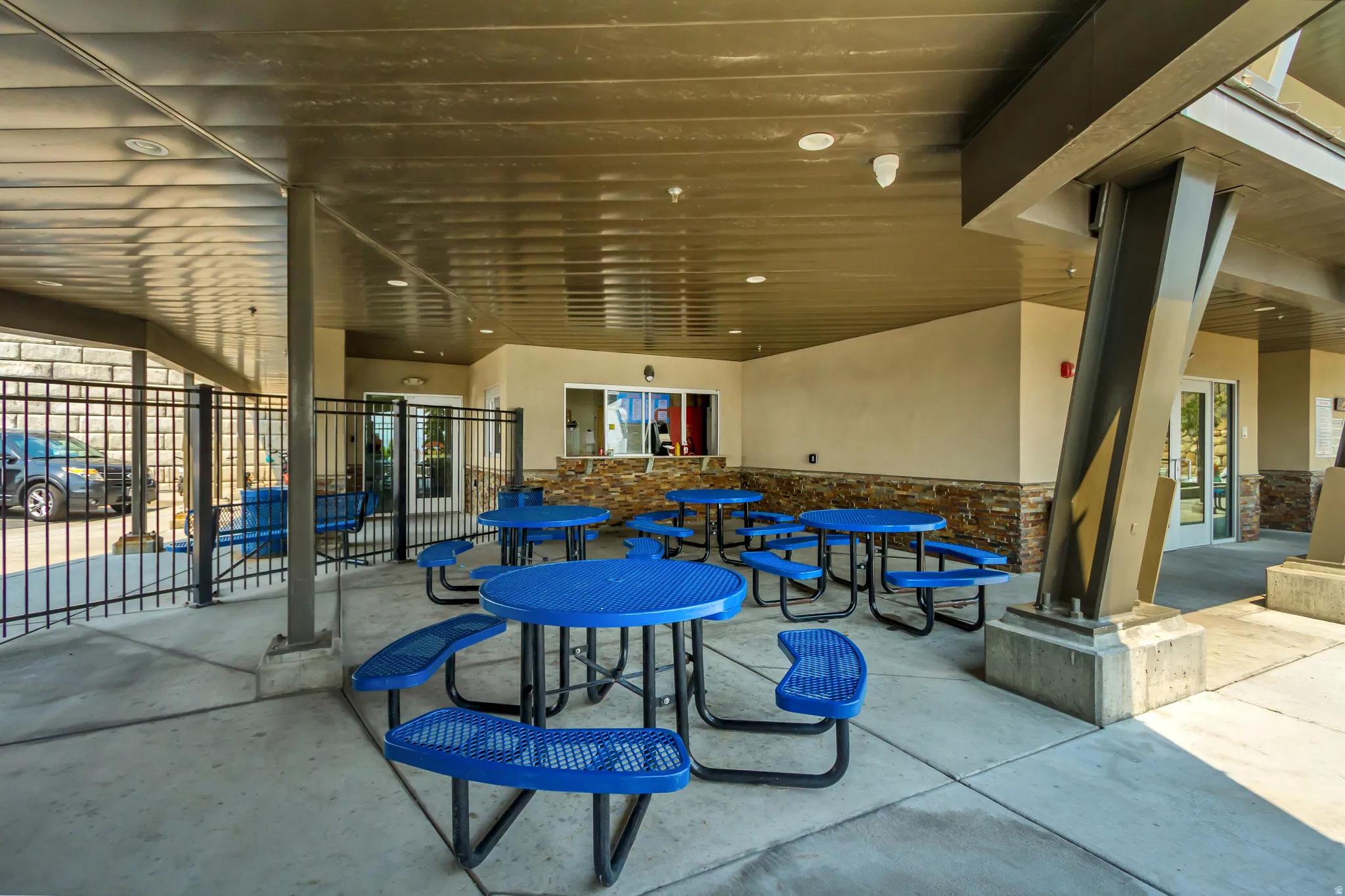 Covered patio area featuring multiple blue picnic tables, a stone-accented exterior wall, and a large service window