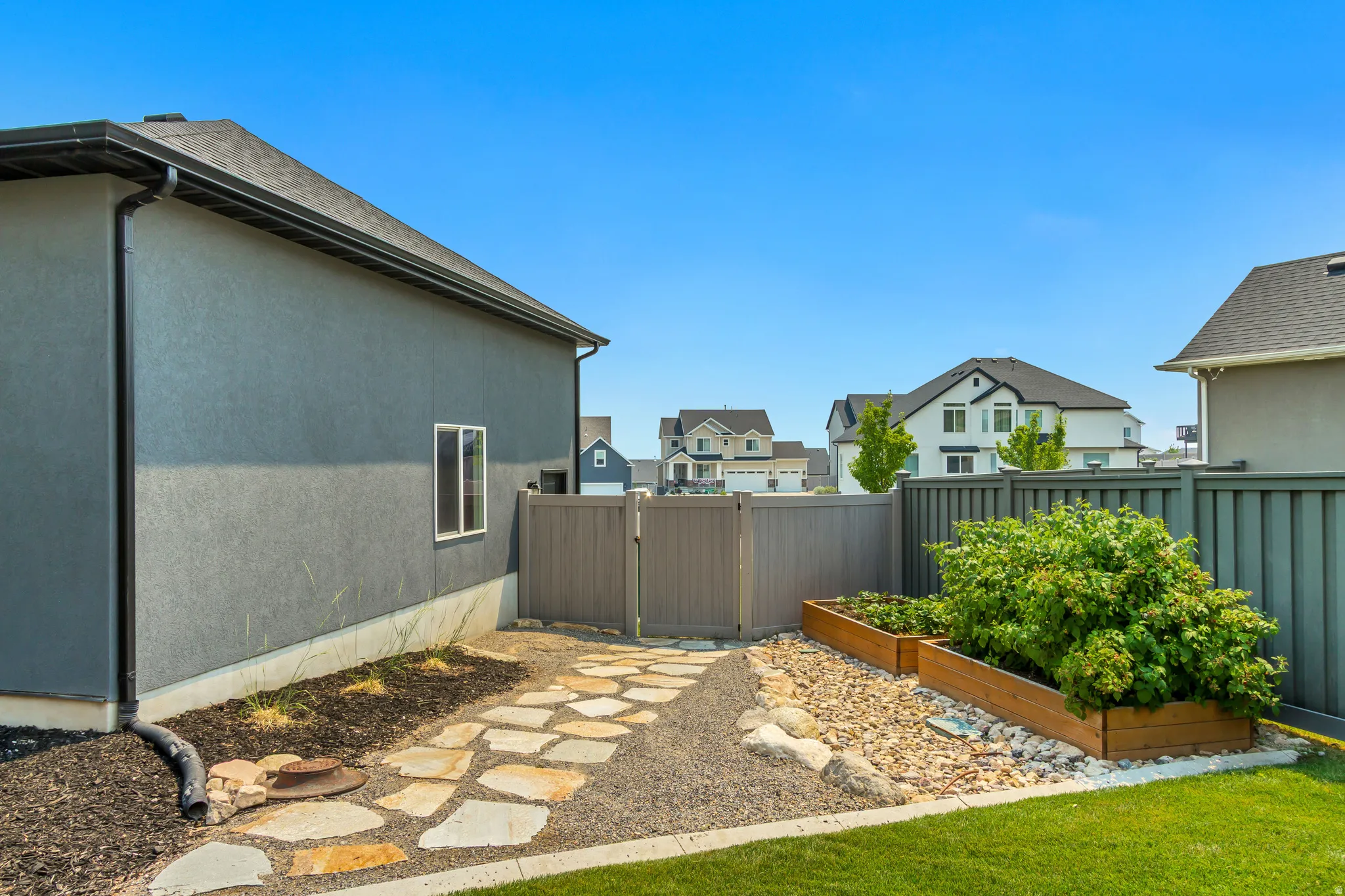 Exterior side yard featuring a stucco finish, stone pathway, gravel landscaping, raised garden beds, and a privacy fence