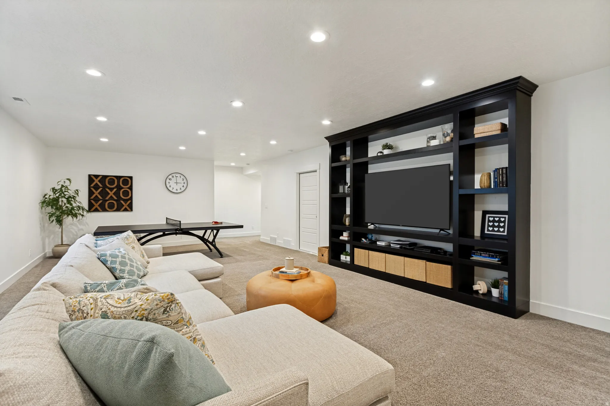 Spacious entertainment area featuring a built-in media center with integrated shelving, recessed lighting, neutral carpeting, and white baseboards
