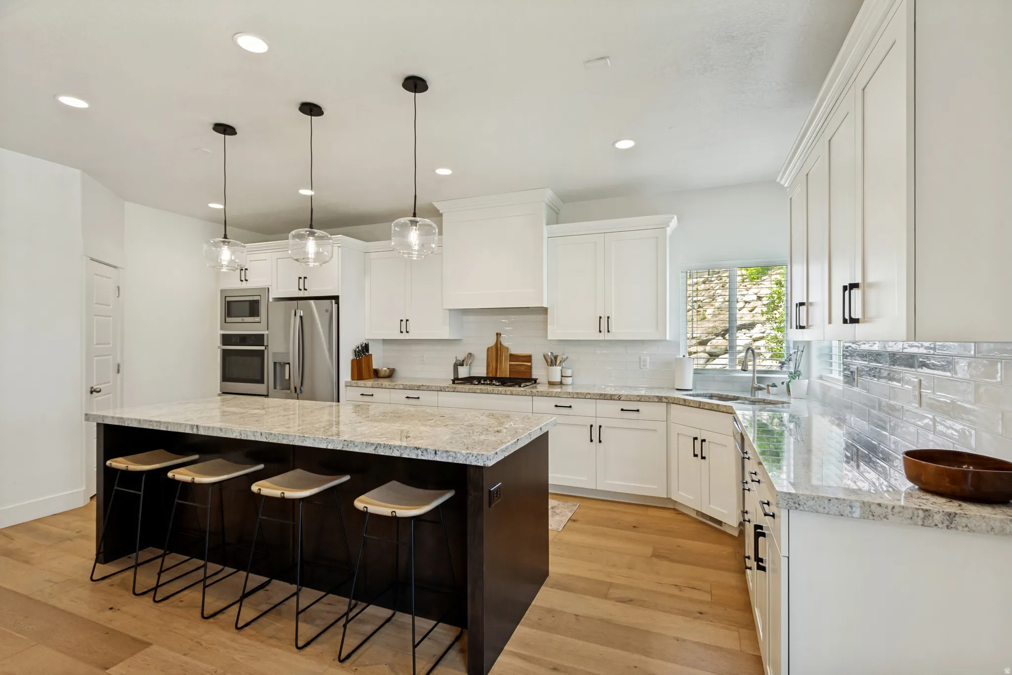 Bright kitchen featuring a dark wood island with light stone countertop, pendant lighting, and light wood-finish flooring