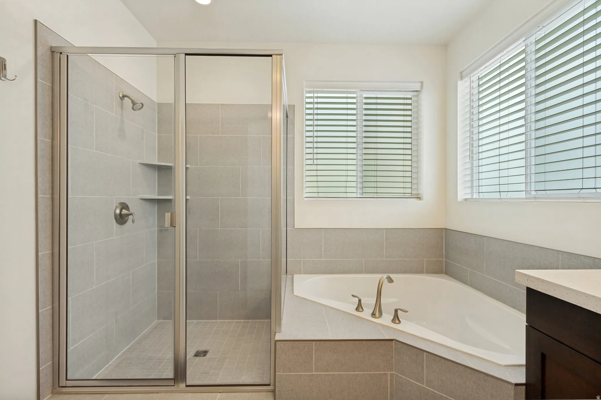 Corner soaking tub with brass fixtures and two windows featuring blinds