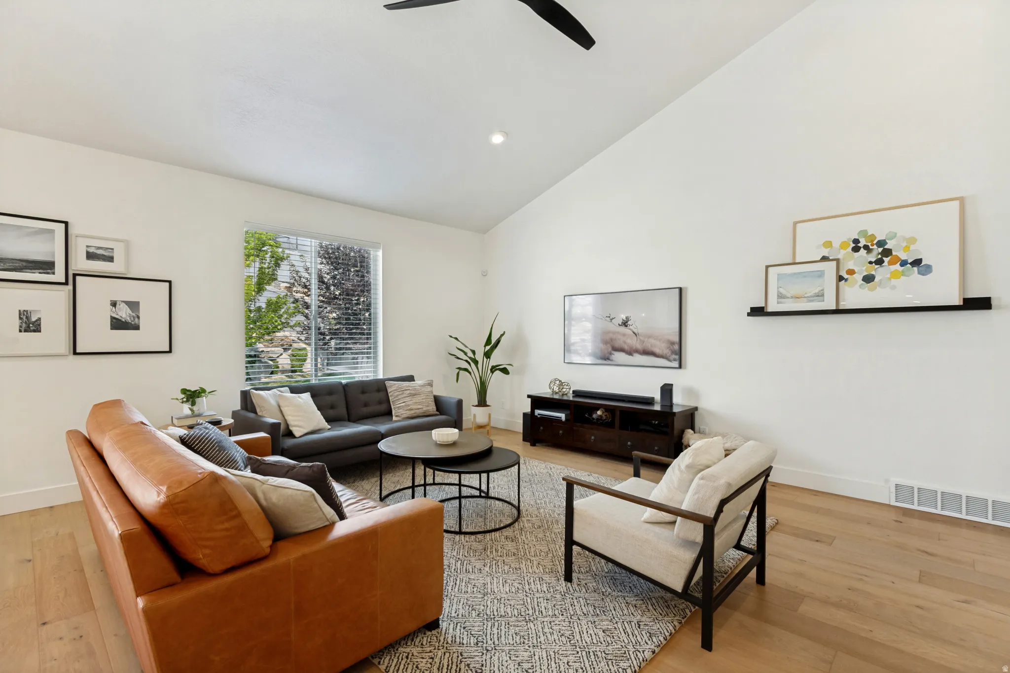 Living area featuring vaulted ceilings, light wood-finish flooring, recessed lighting, a ceiling fan, and a large window with horizontal blinds