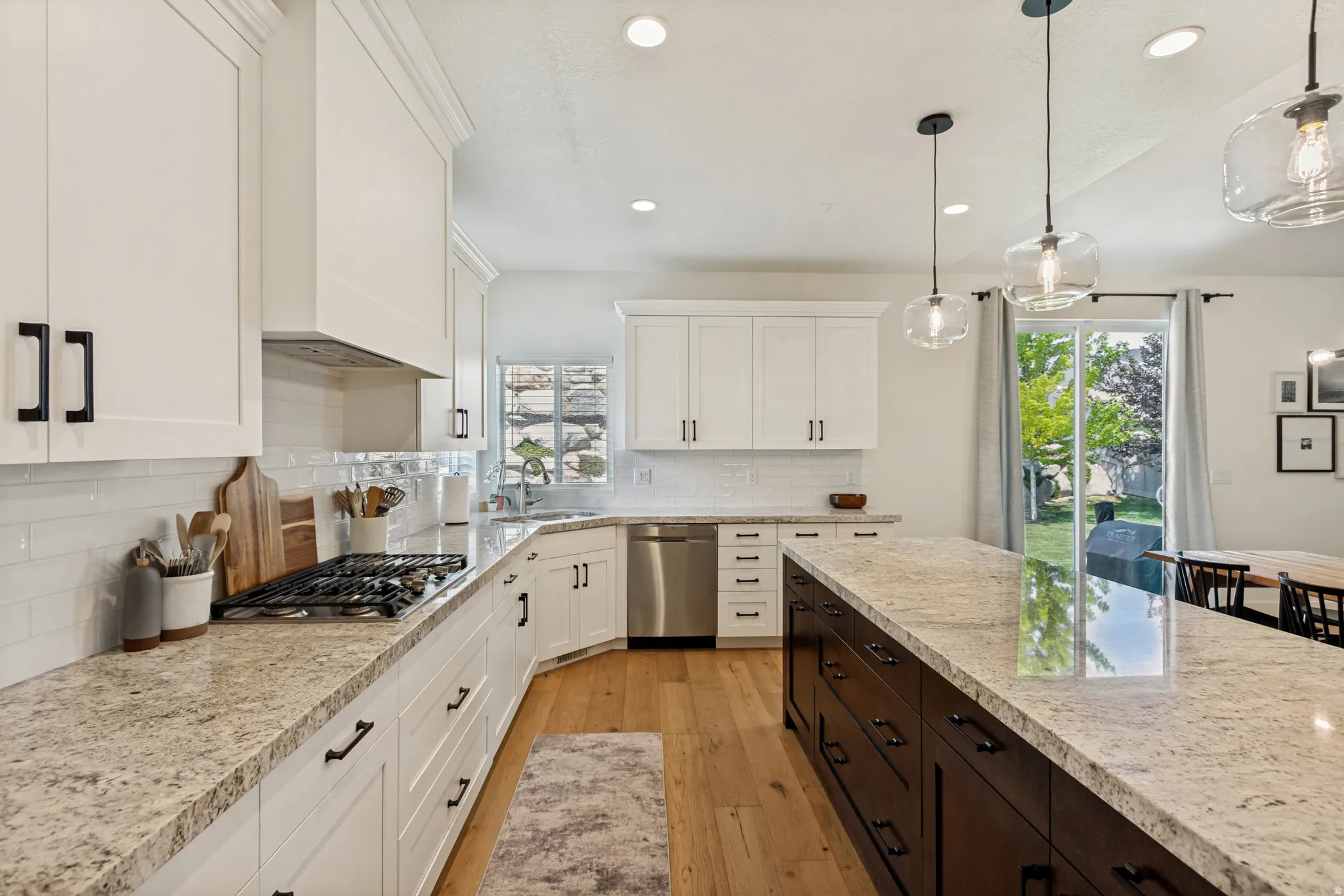 Spacious kitchen featuring white shaker cabinetry, light-toned granite countertops, a dark wood-finish island with storage, stainless steel appliances, and wood-finish flooring