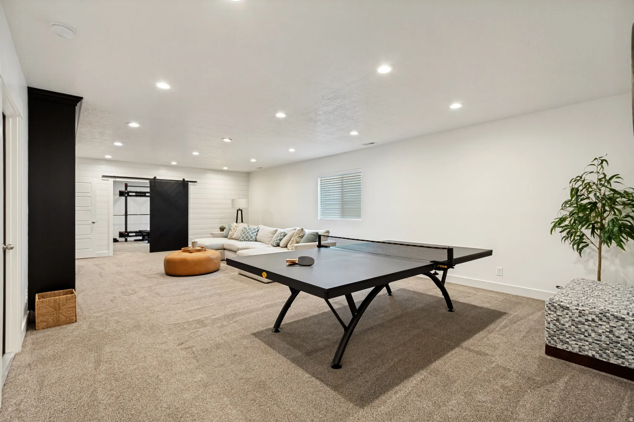 Spacious carpeted room featuring recessed lighting, a white shiplap accent wall, and a black barn door leading to an additional space
