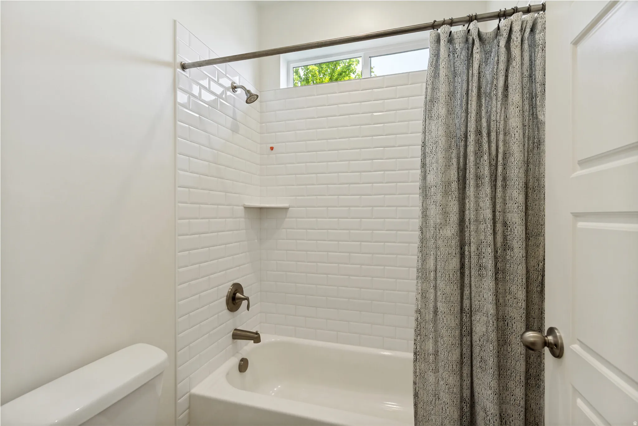 Bathroom featuring a white subway tile surround, built-in tub, and brushed nickel fixtures