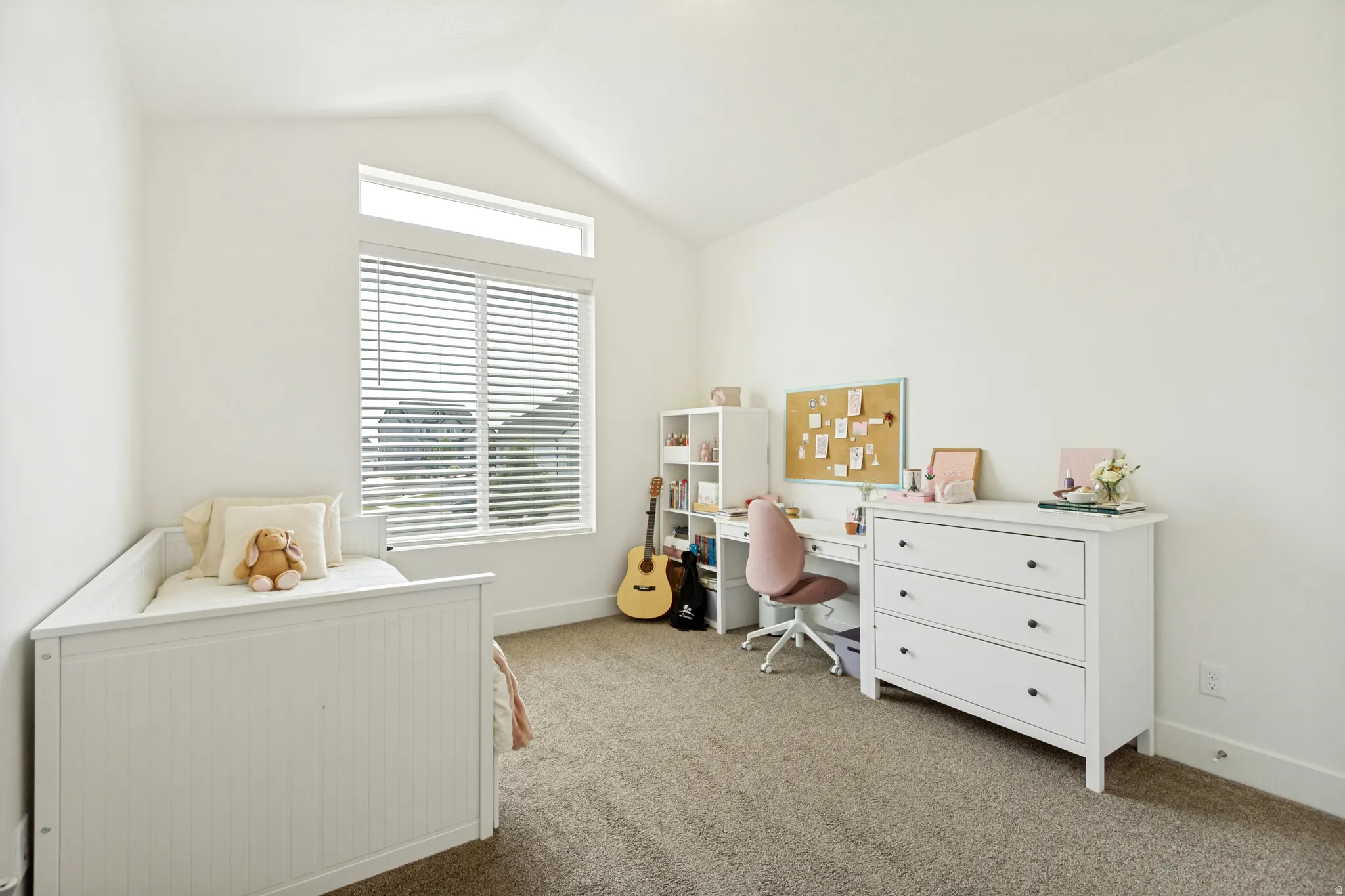 Vaulted ceiling room featuring a large window with blinds, an upper transom window, and neutral-toned carpet