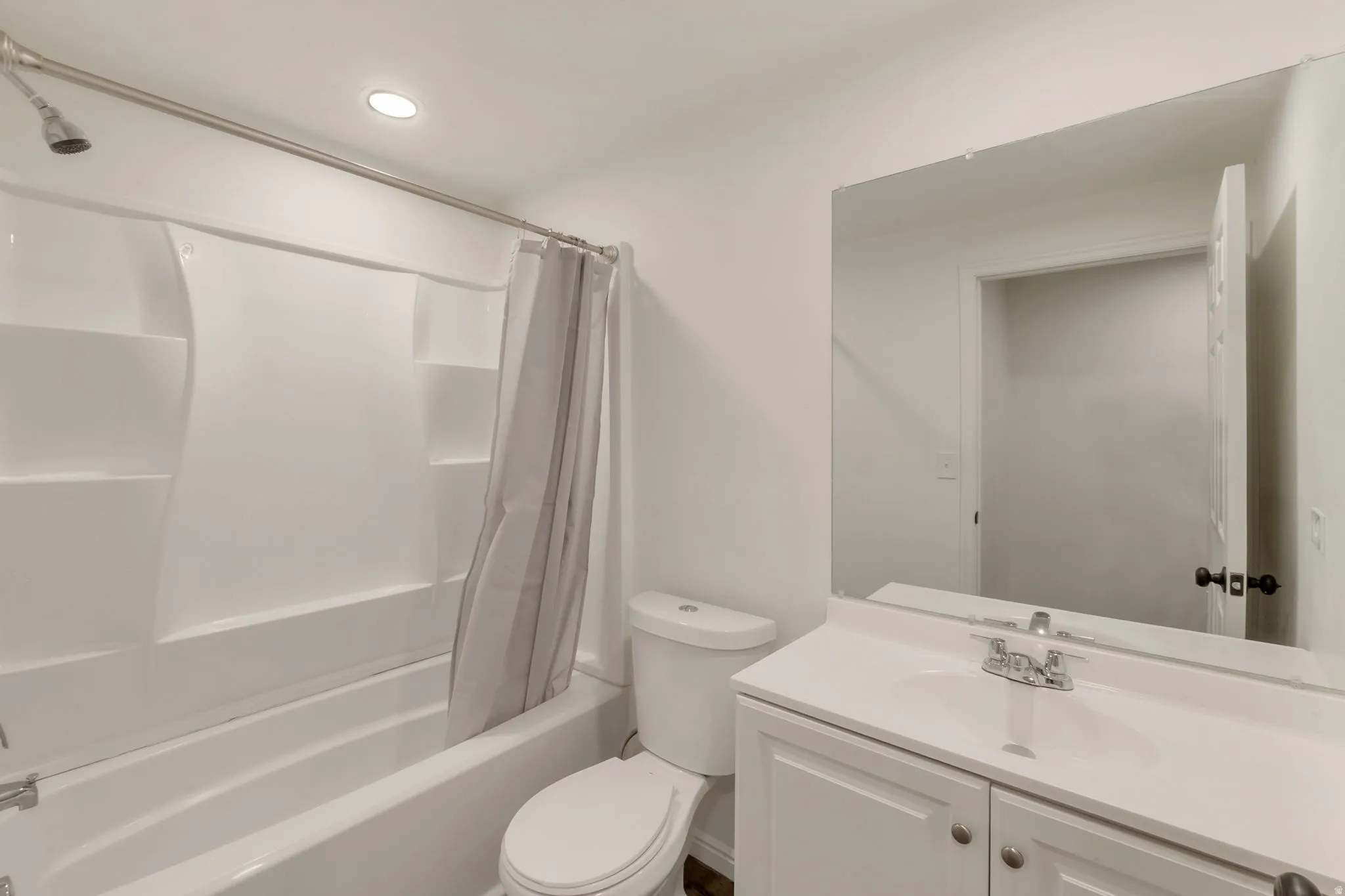 Bathroom featuring a white vanity with integrated sink, a frameless wall mirror, and a full-sized bathtub with an overhead shower