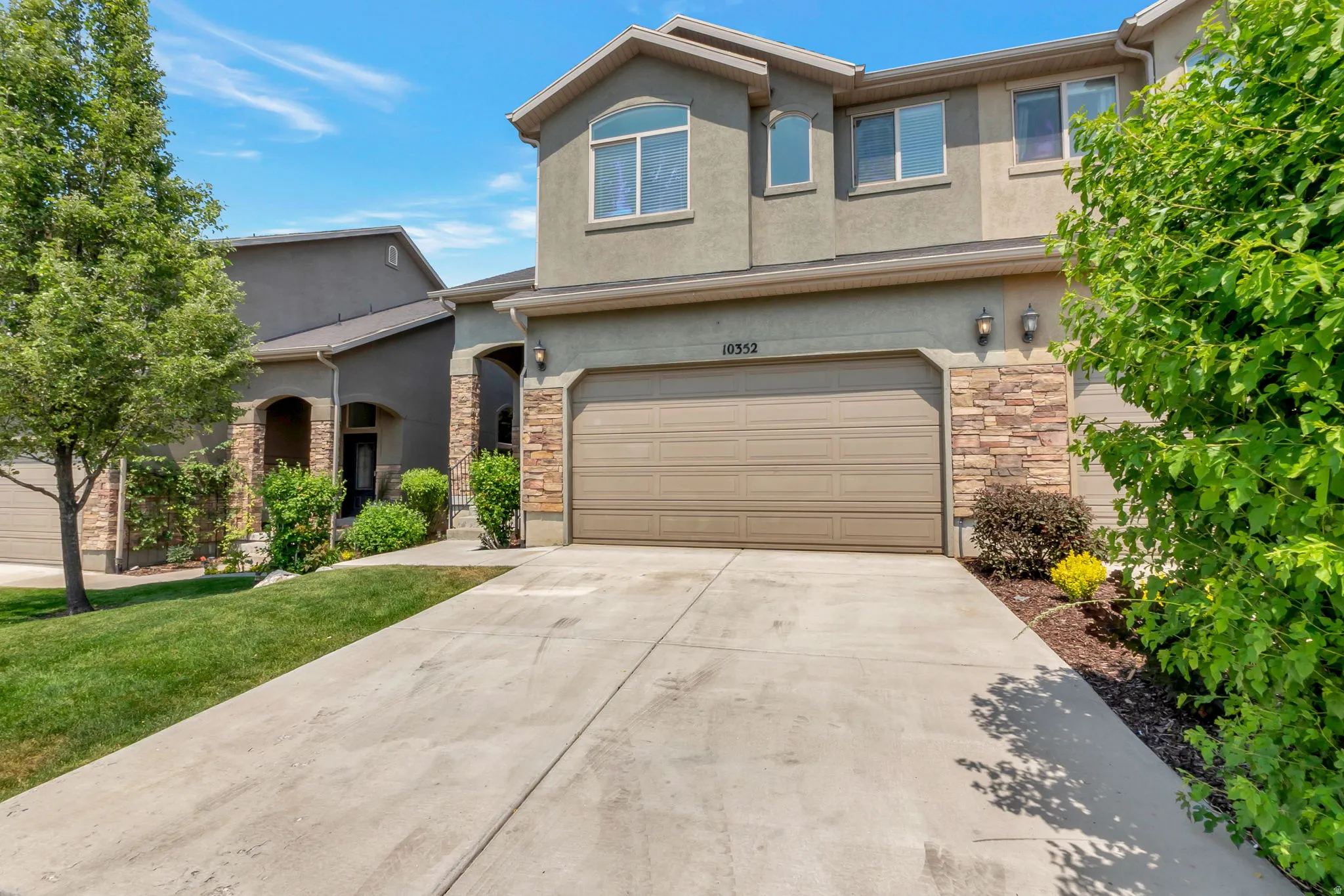 Stucco and stone facade with an integrated garage, paved driveway, and established landscaping