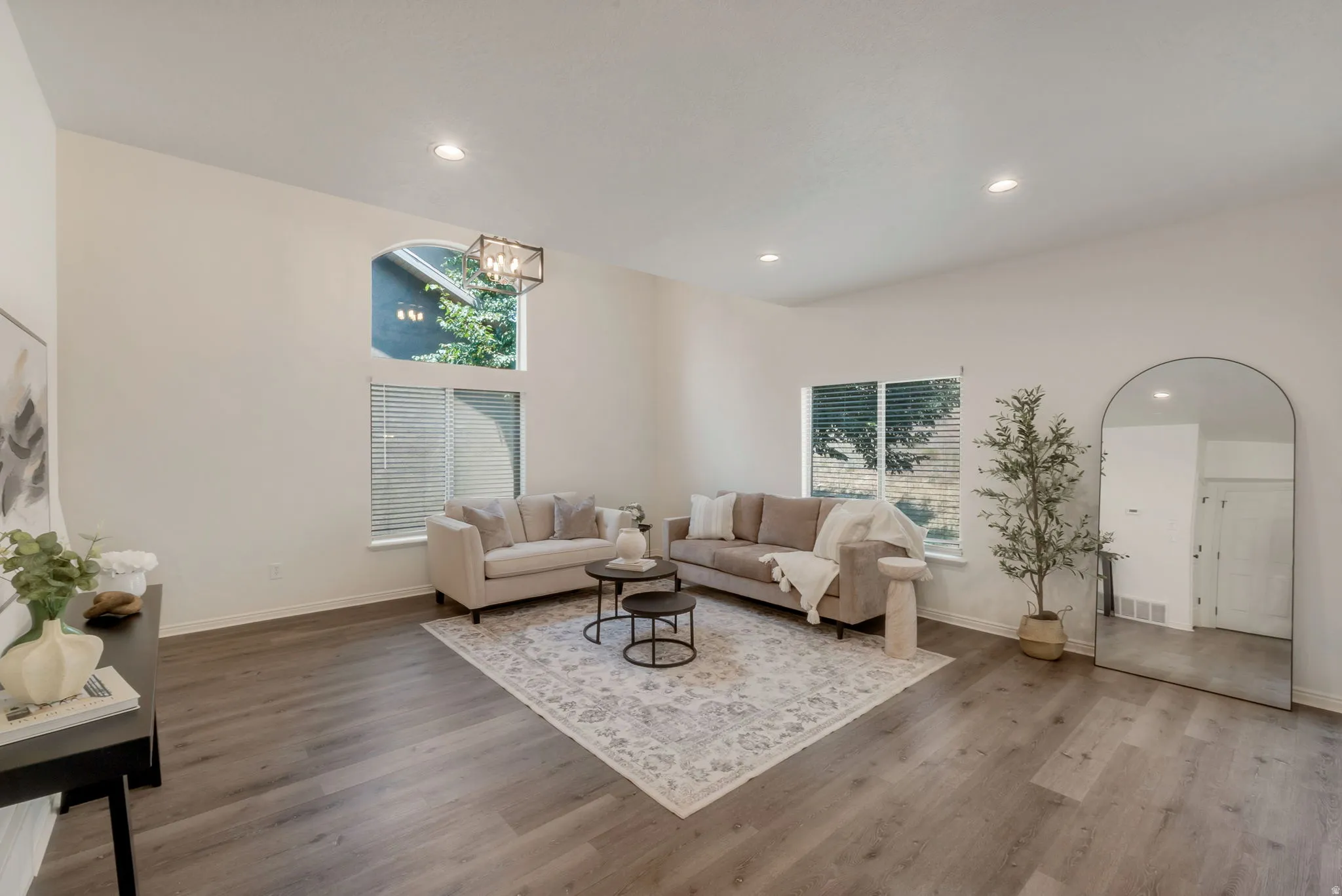 Spacious living area featuring high vaulted ceilings, recessed lighting, wood-finish flooring, and multiple windows including an arched architectural window