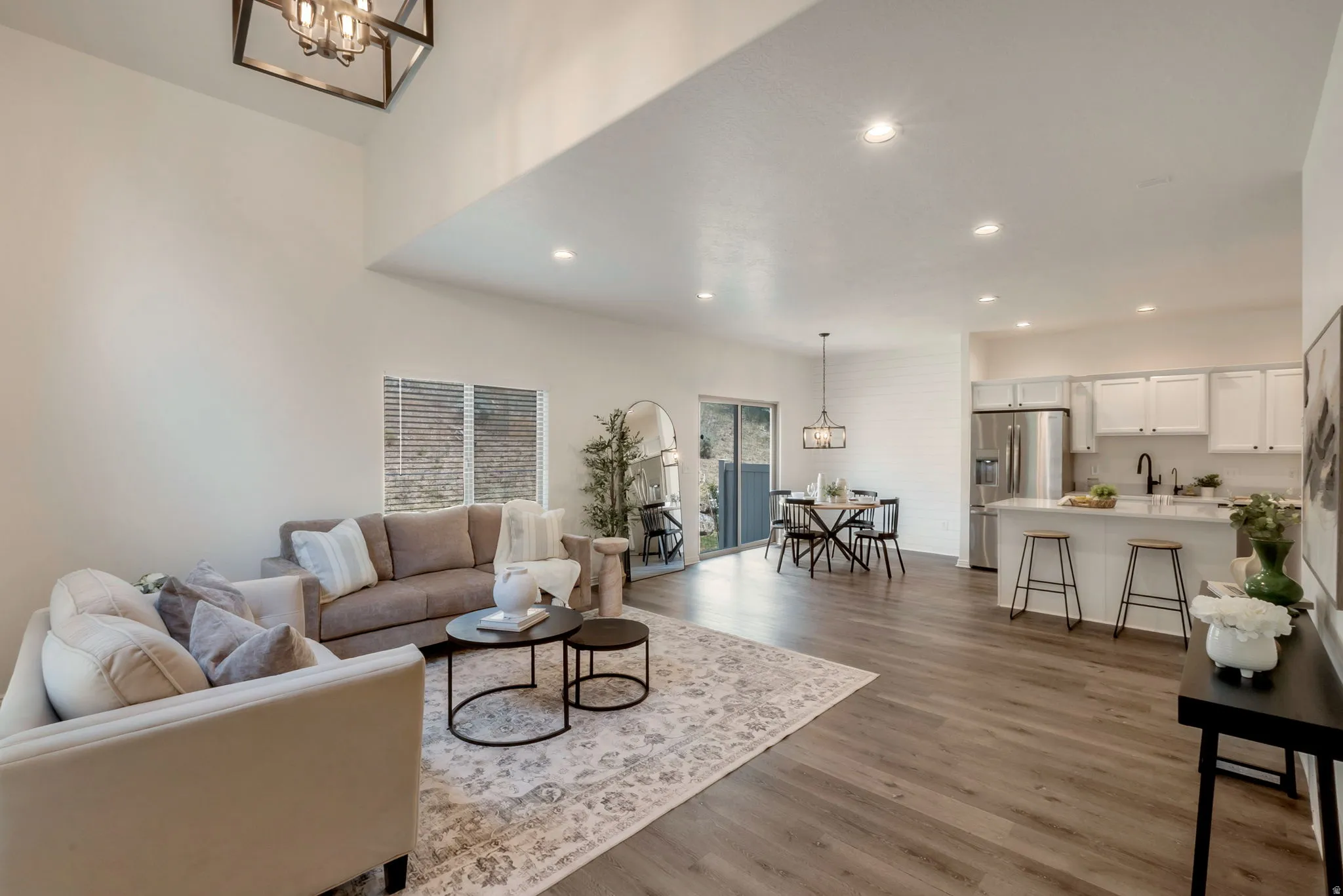 Open-concept living area featuring high vaulted ceilings, recessed lighting, wood-finish flooring, a kitchen island with seating, and stainless steel appliances