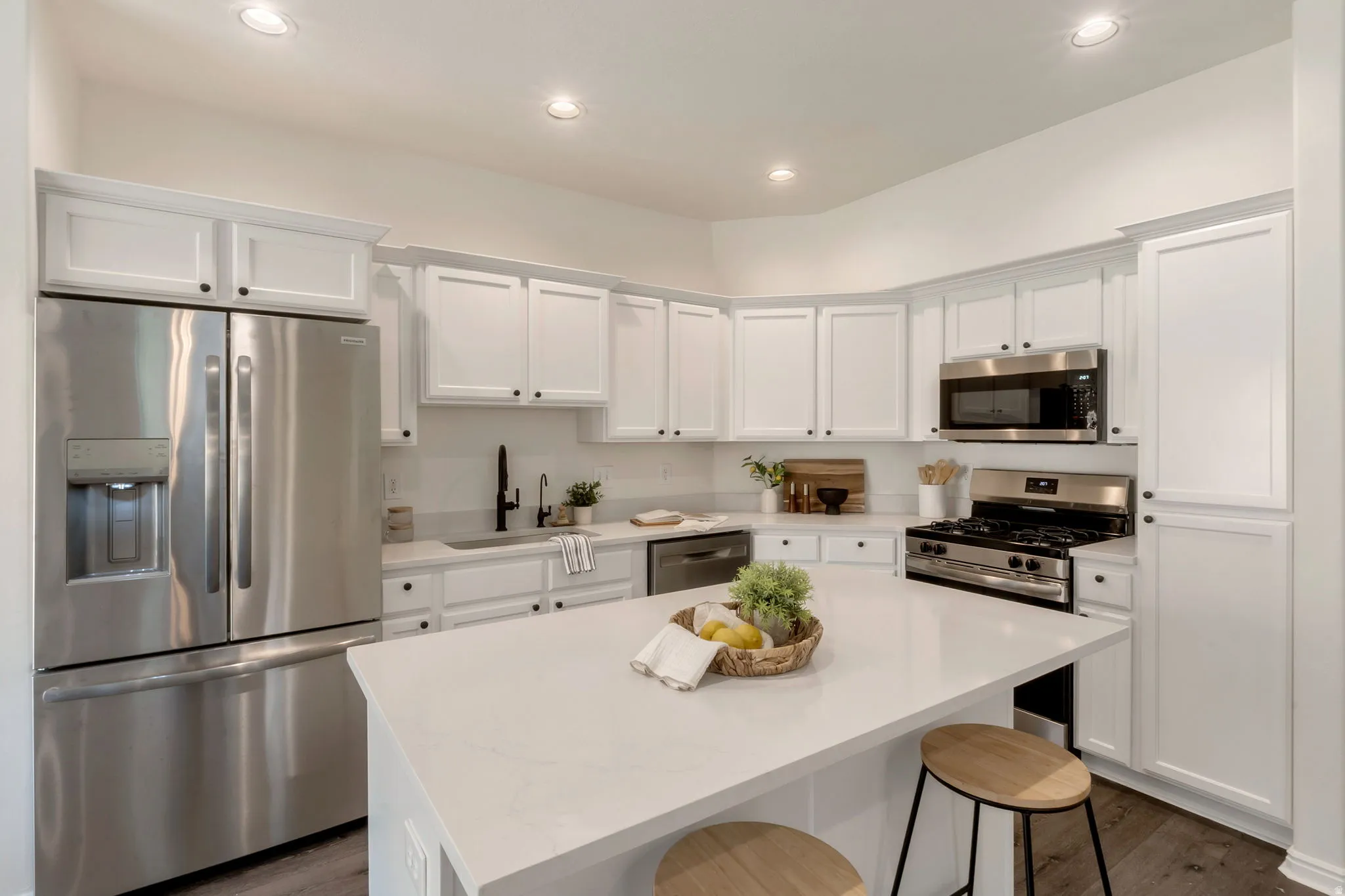 Modern kitchen featuring white cabinetry with black hardware, stainless steel appliances, a white countertop island, recessed lighting, and wood-finish flooring