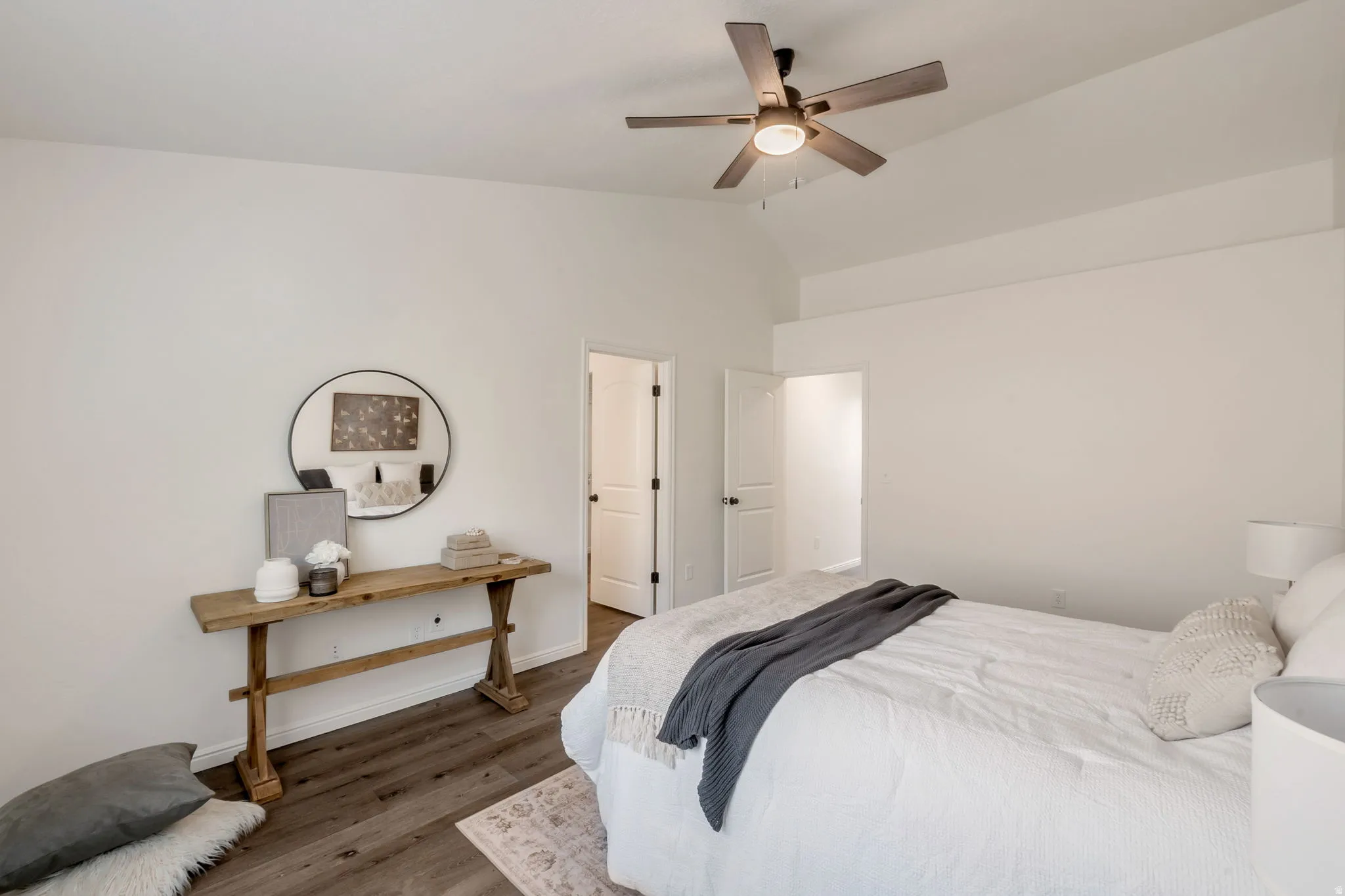 Spacious room featuring vaulted ceilings, a contemporary ceiling fan with integrated lighting, wood-finish flooring, and white paneled interior doors