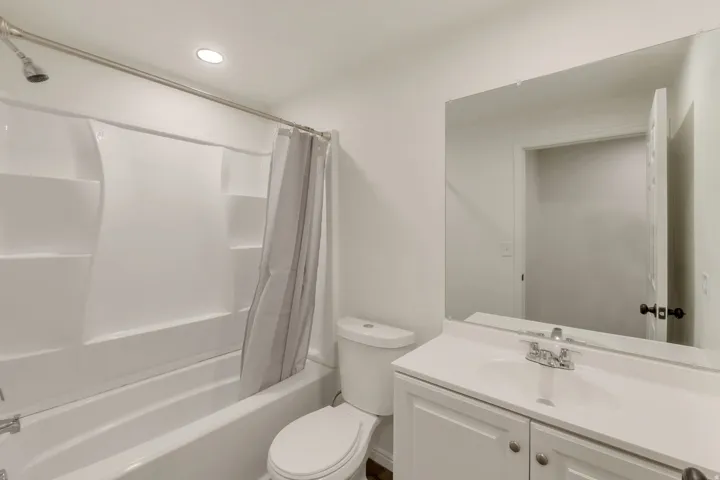 Bathroom featuring a white vanity with integrated sink, a frameless wall mirror, and a full-sized bathtub with an overhead shower