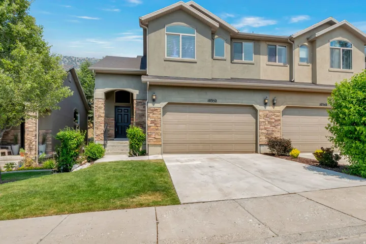 Stucco exterior featuring stone accents, a covered entry, and an attached two-car garage