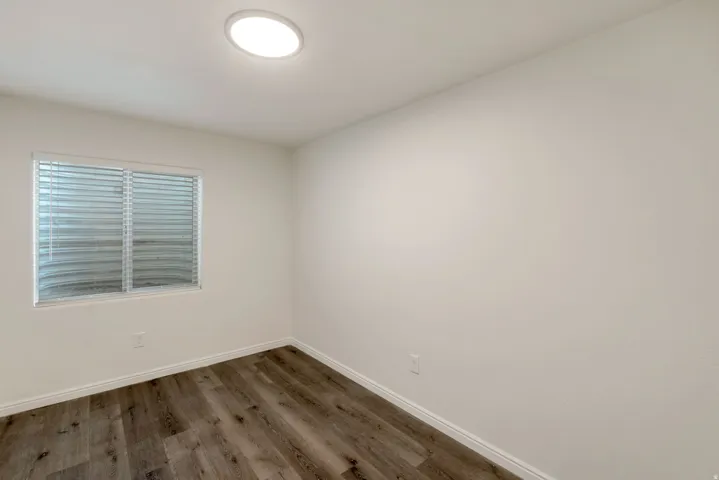Room featuring wood-finish flooring, white baseboards, a single window with blinds, and a flush-mount ceiling light