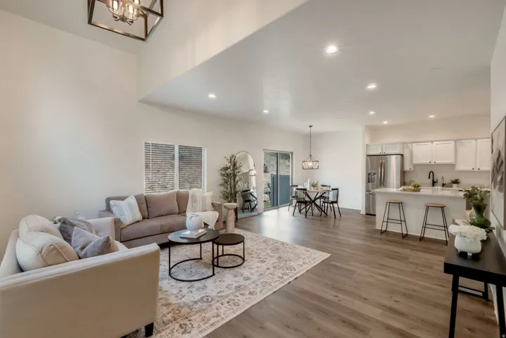 Open-concept living area featuring high vaulted ceilings, recessed lighting, wood-finish flooring, a kitchen island with seating, and stainless steel appliances