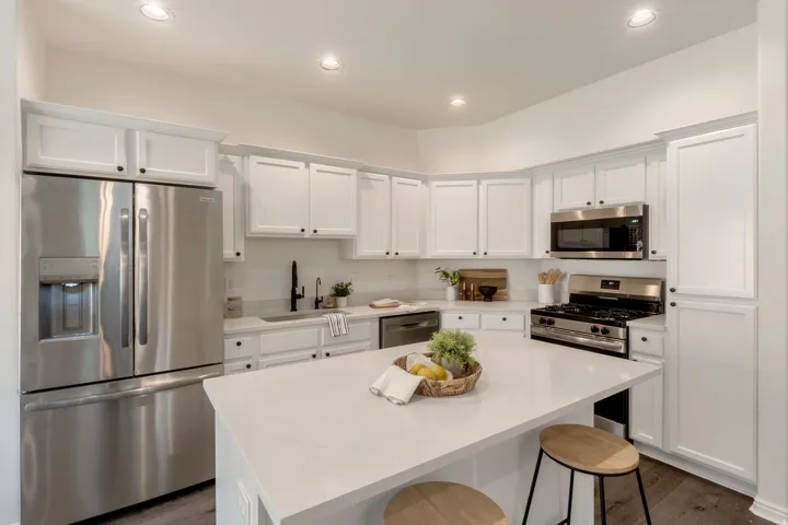 Modern kitchen featuring white cabinetry with black hardware, stainless steel appliances, a white countertop island, recessed lighting, and wood-finish flooring