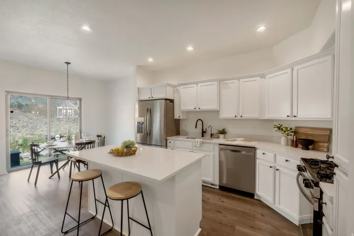 Kitchen featuring white cabinetry, stainless steel appliances, a center island with countertop seating, recessed lighting, and wood-finish flooring