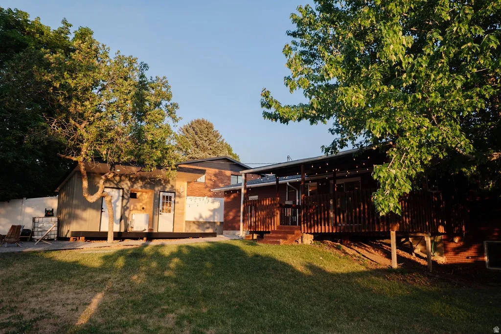 Expansive backyard featuring a lush lawn, mature trees, and a spacious wood-finish deck with a covered area
