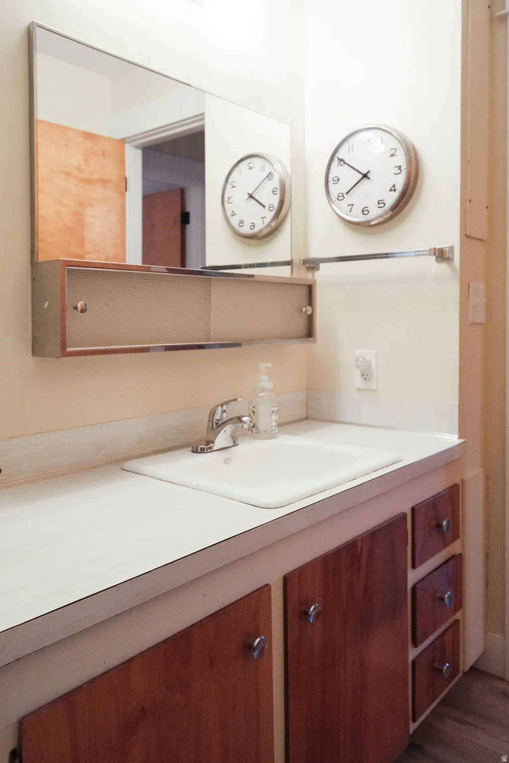 Bathroom vanity featuring a white countertop with an integrated sink, chrome faucet, and wood-finish cabinetry