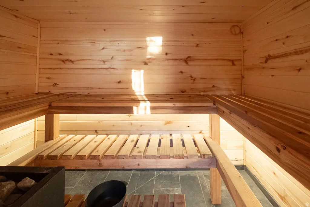 Sauna room featuring natural wood paneling, multi-level slatted wooden benches, and dark stone tile flooring