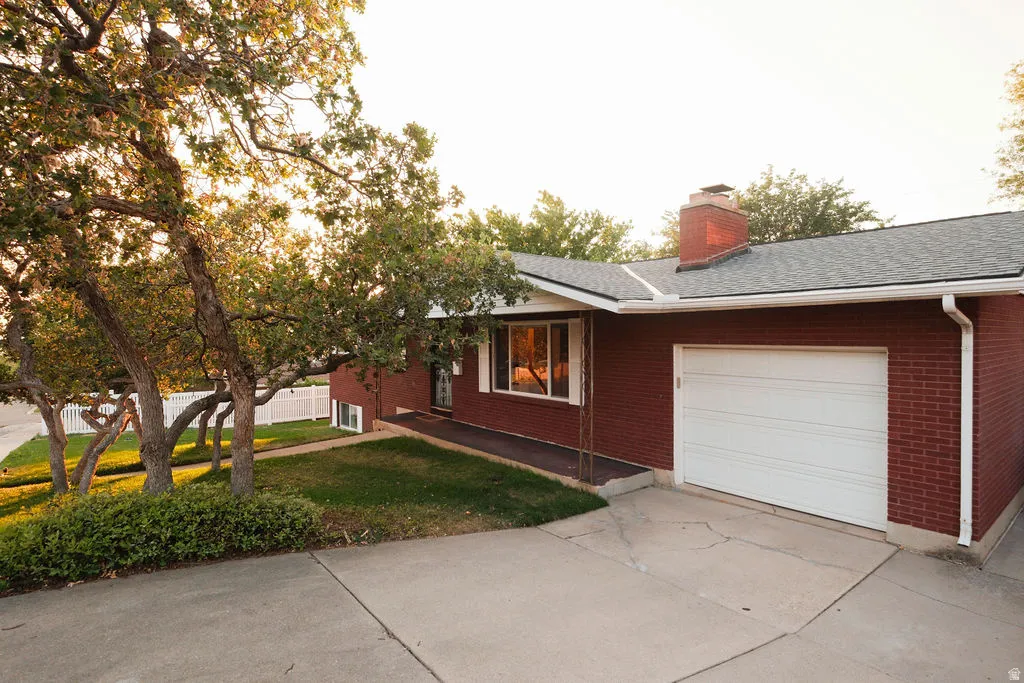 Red brick exterior featuring a white garage door, asphalt shingle roof, and a red brick chimney
