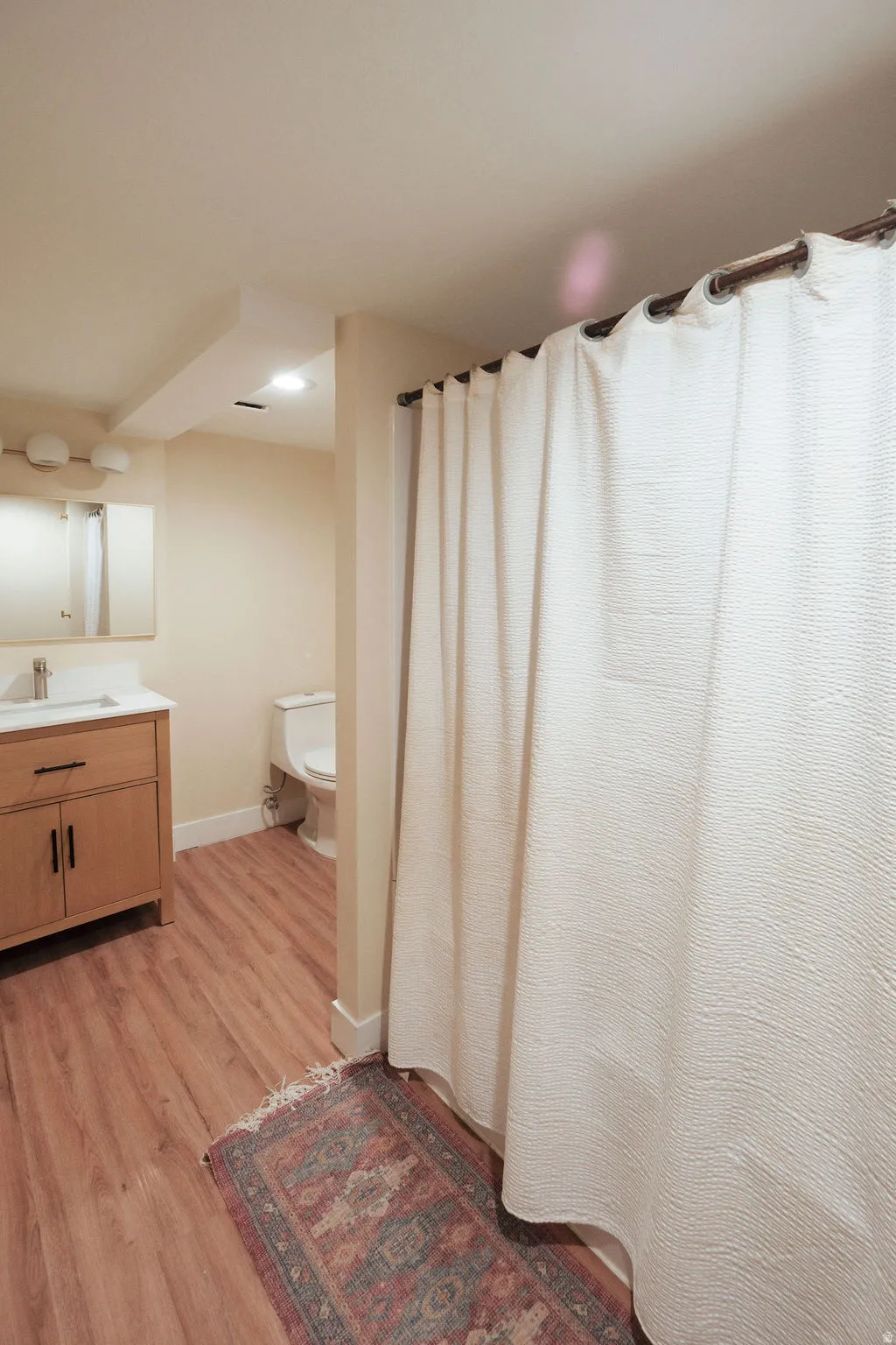Bathroom featuring wood-finish flooring, a vanity with under-sink storage, a wall-mounted mirror, and a white toilet