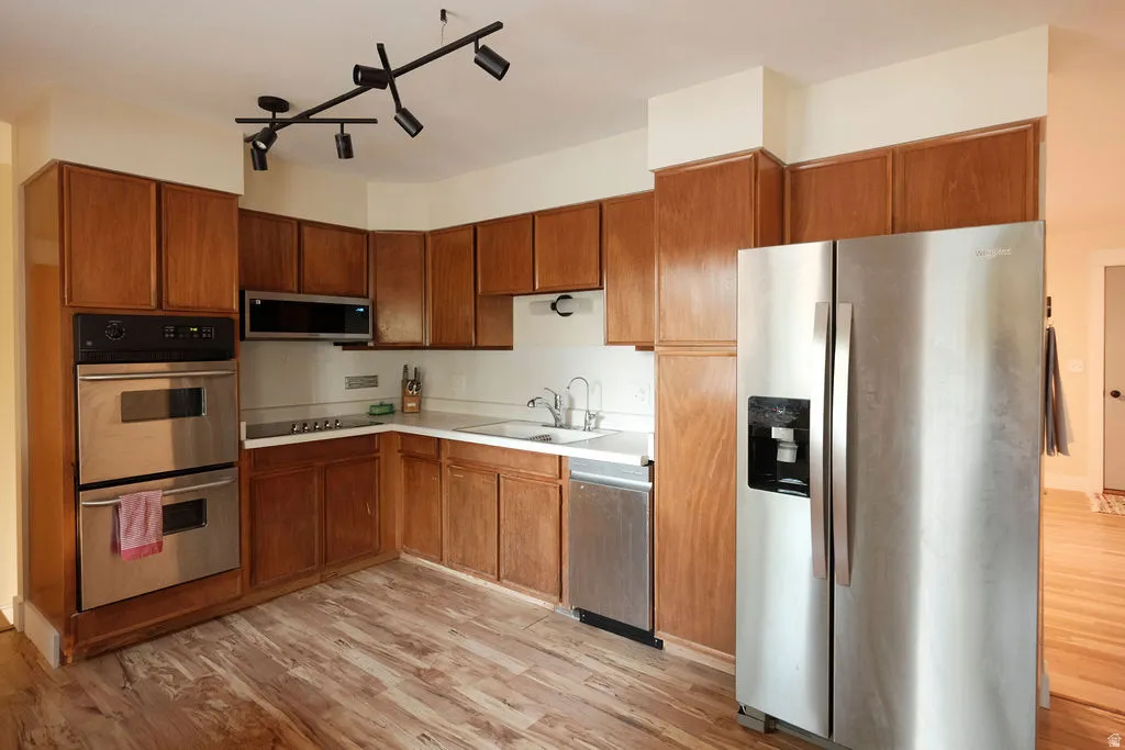 Kitchen featuring wood-finish cabinetry, stainless steel double wall ovens, a stainless steel microwave, a built-in stainless steel dishwasher, and wood-finish flooring
