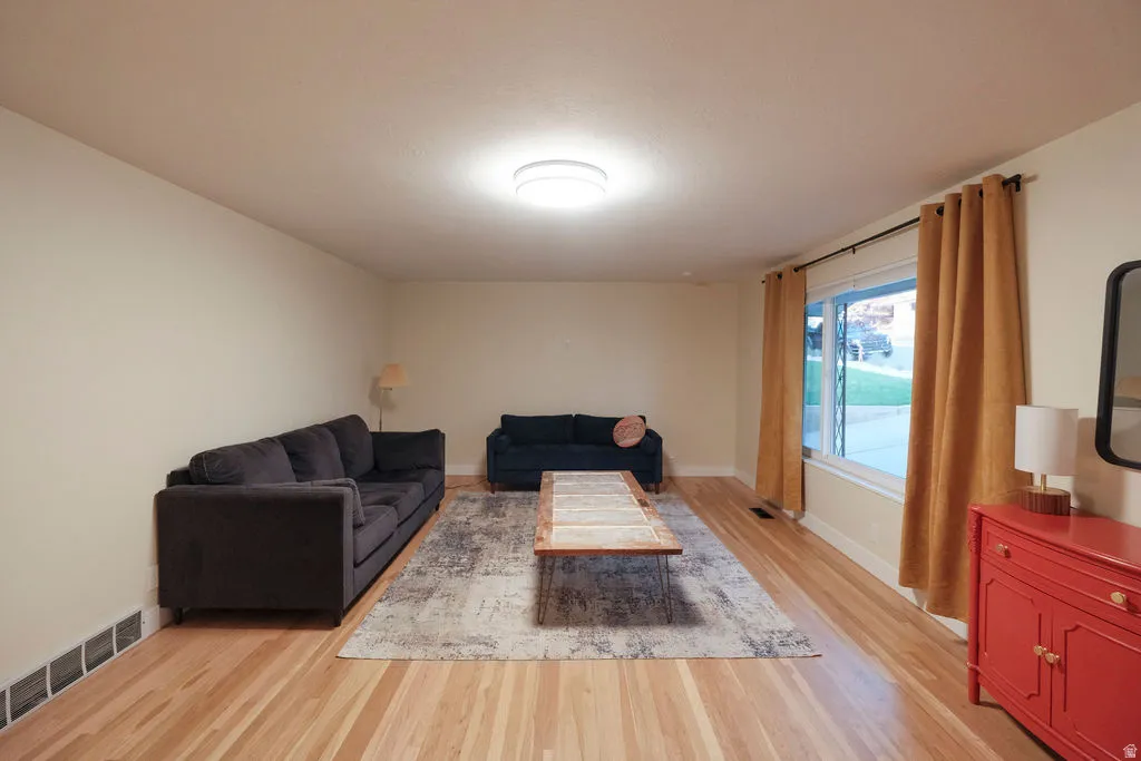 Spacious living area featuring light wood-finish flooring, neutral wall tones, and a large window providing natural light