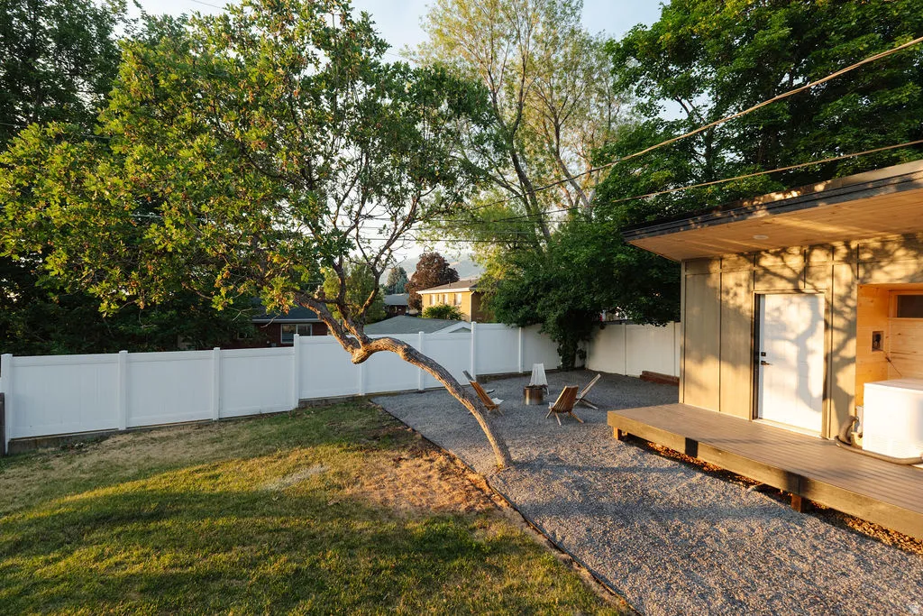 Exterior featuring a wooden deck with an overhang, gravel patio, white privacy fence, and a mature tree