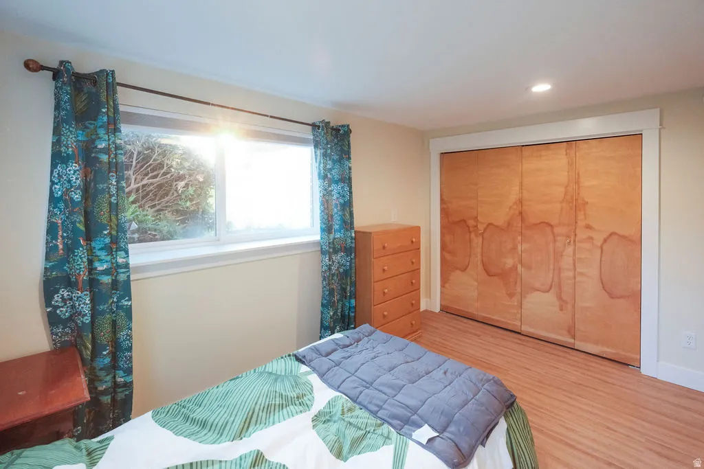 Bedroom featuring wood-finish flooring, a window with exterior landscaping, a recessed ceiling light, and bi-fold closet doors with white trim