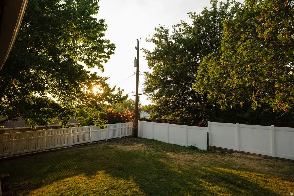 Expansive backyard featuring a manicured lawn, a white picket fence, a solid white privacy fence, and mature trees