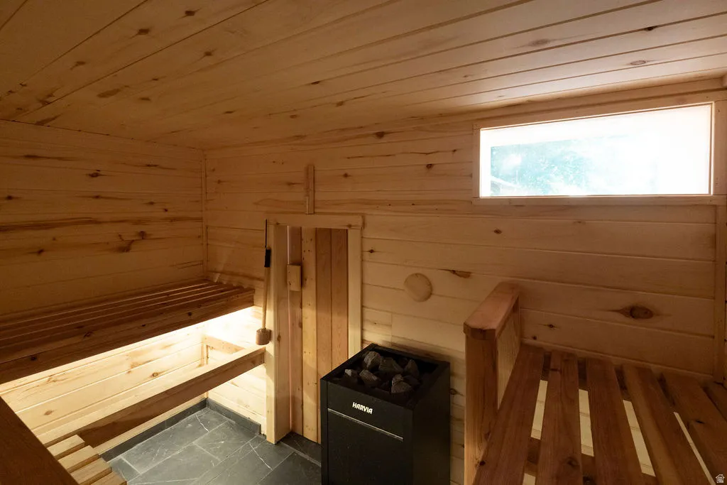 Custom sauna featuring light wood paneling, multi-level wooden benches, slate tile flooring, a wall-mounted heater, and an integrated transom window