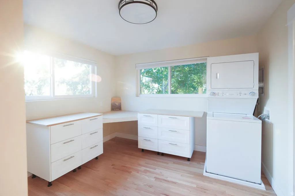 Spacious room featuring wood-finish flooring, multiple windows, a built-in corner desk, and white cabinetry with wood-look countertops