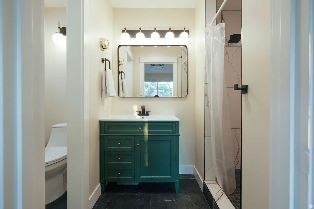 Bathroom featuring a dark green vanity with brass-finish hardware, a rectangular mirror, and a five-light vanity fixture