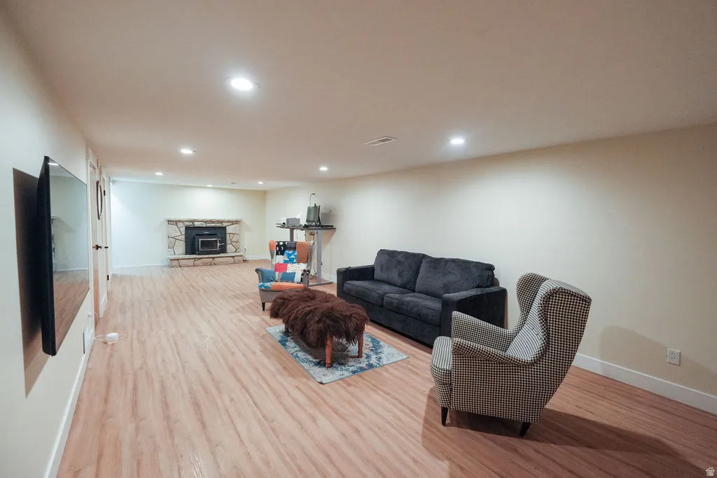 Spacious room featuring wood-finish flooring, recessed lighting, and a stone-clad fireplace with a wood-burning insert