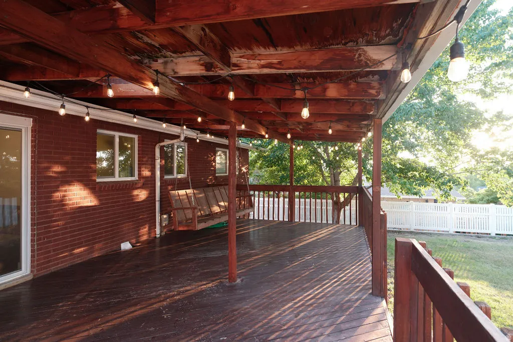 Expansive covered deck featuring string lighting, wood-finish flooring, and a swing