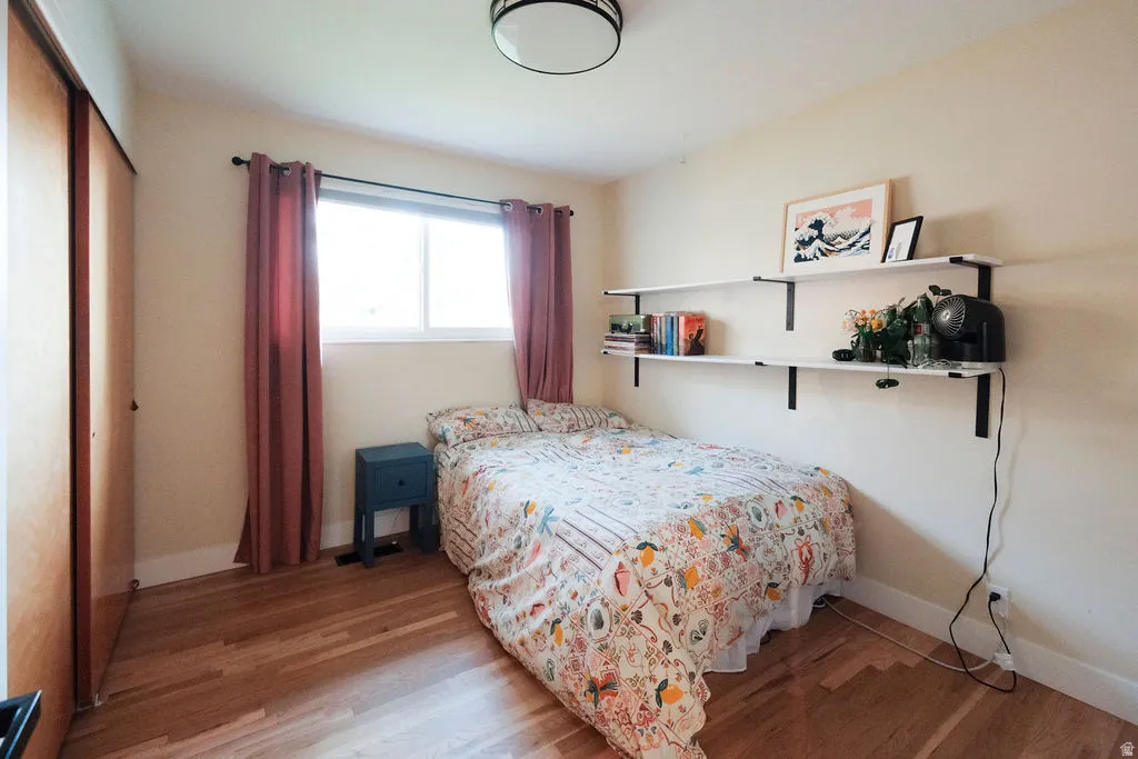 Hardwood flooring throughout featuring a window with natural light, two floating shelves, a ceiling-mounted light fixture, and a built-in closet with sliding wood-finish doors
