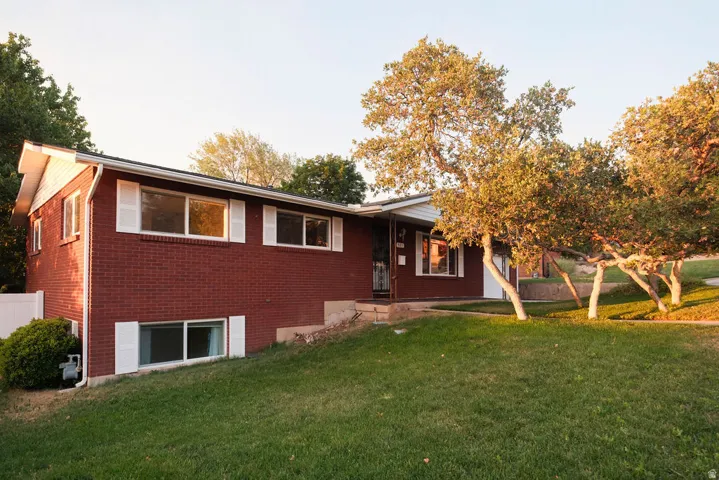 Red brick exterior with white decorative shutters, a covered entry, and mature trees