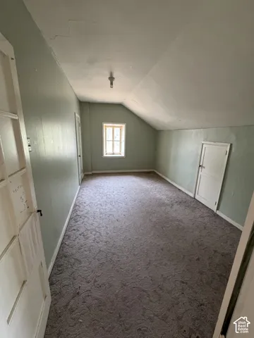 Spacious room featuring sloped ceilings, a single window providing natural illumination, and a patterned carpet floor