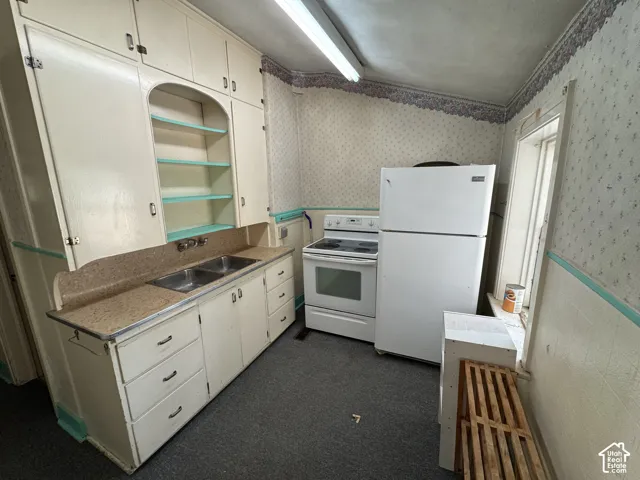 Kitchen featuring built-in cabinetry with open shelving, dual basin sink, integrated countertop, white range, and white refrigerator