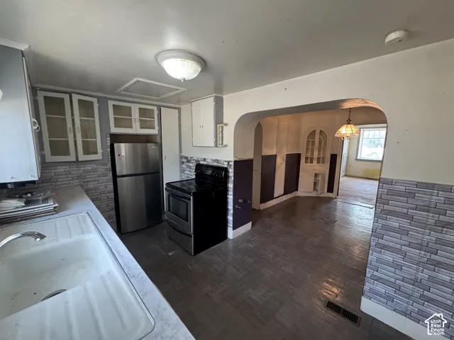 Kitchen featuring white cabinetry with glass inserts, stainless steel refrigerator, black range, and an integrated sink with a chrome faucet