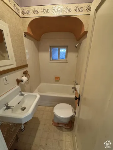 Bathroom featuring a white porcelain pedestal sink with separate hot and cold taps, a built-in bathtub with shower, and an arched alcove