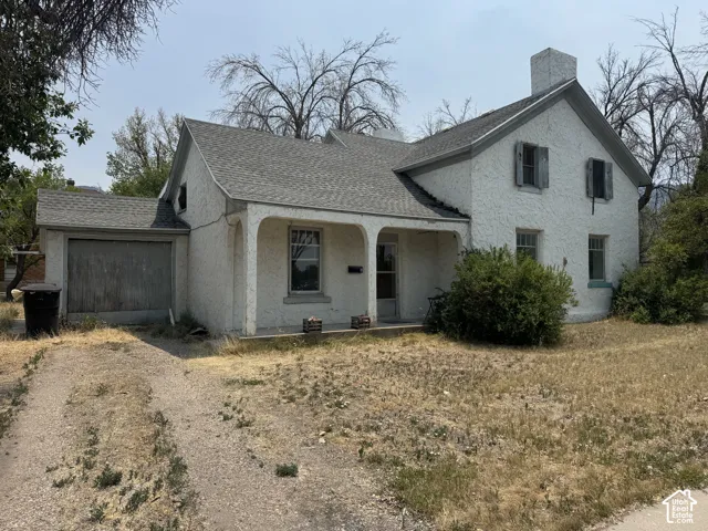 White stucco exterior featuring a covered porch entrance, attached garage, and multi-pane windows