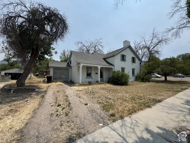 White stucco exterior featuring a covered entry porch, multiple window openings with shutters, and an attached single-car garage