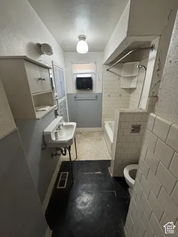 Bathroom featuring a wall-mounted sink, built-in storage cabinetry, tiled bathtub surround, and a toilet