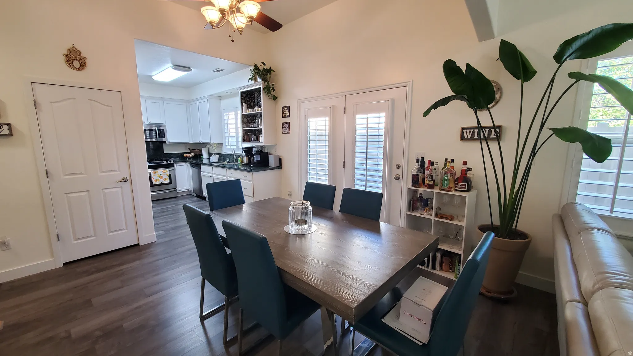 Vaulted ceilings enhance this dining area, featuring wood-finish flooring and French doors with louvered blinds