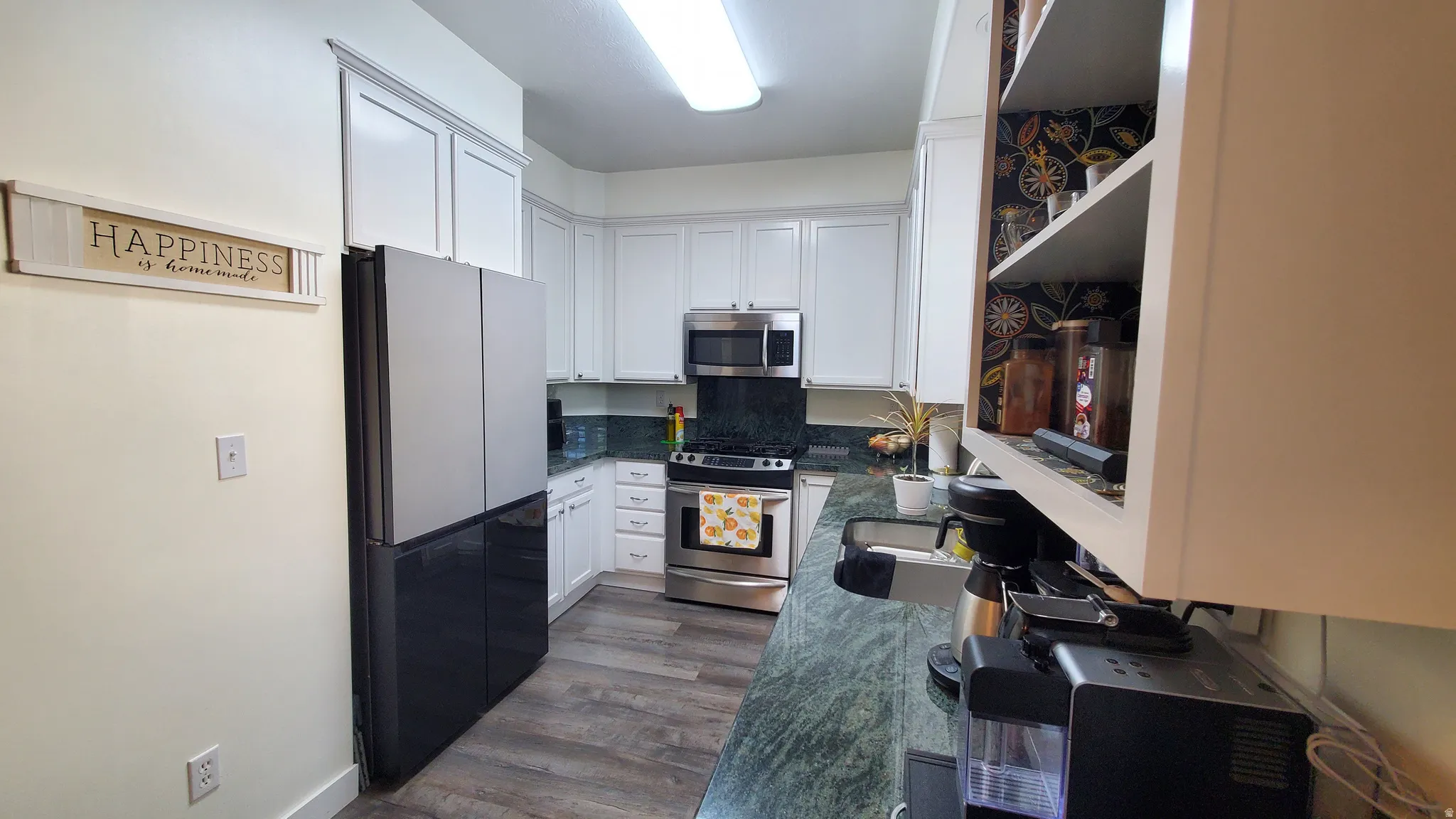 Galley kitchen featuring white cabinetry, dark green countertops, stainless steel appliances, and wood-finish flooring
