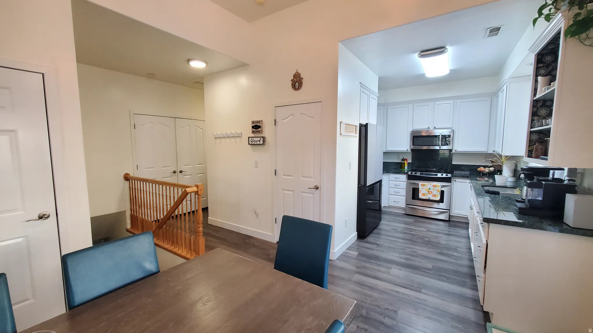 Modern kitchen featuring white shaker-style cabinetry, dark countertops, stainless steel appliances, and wood-finish flooring